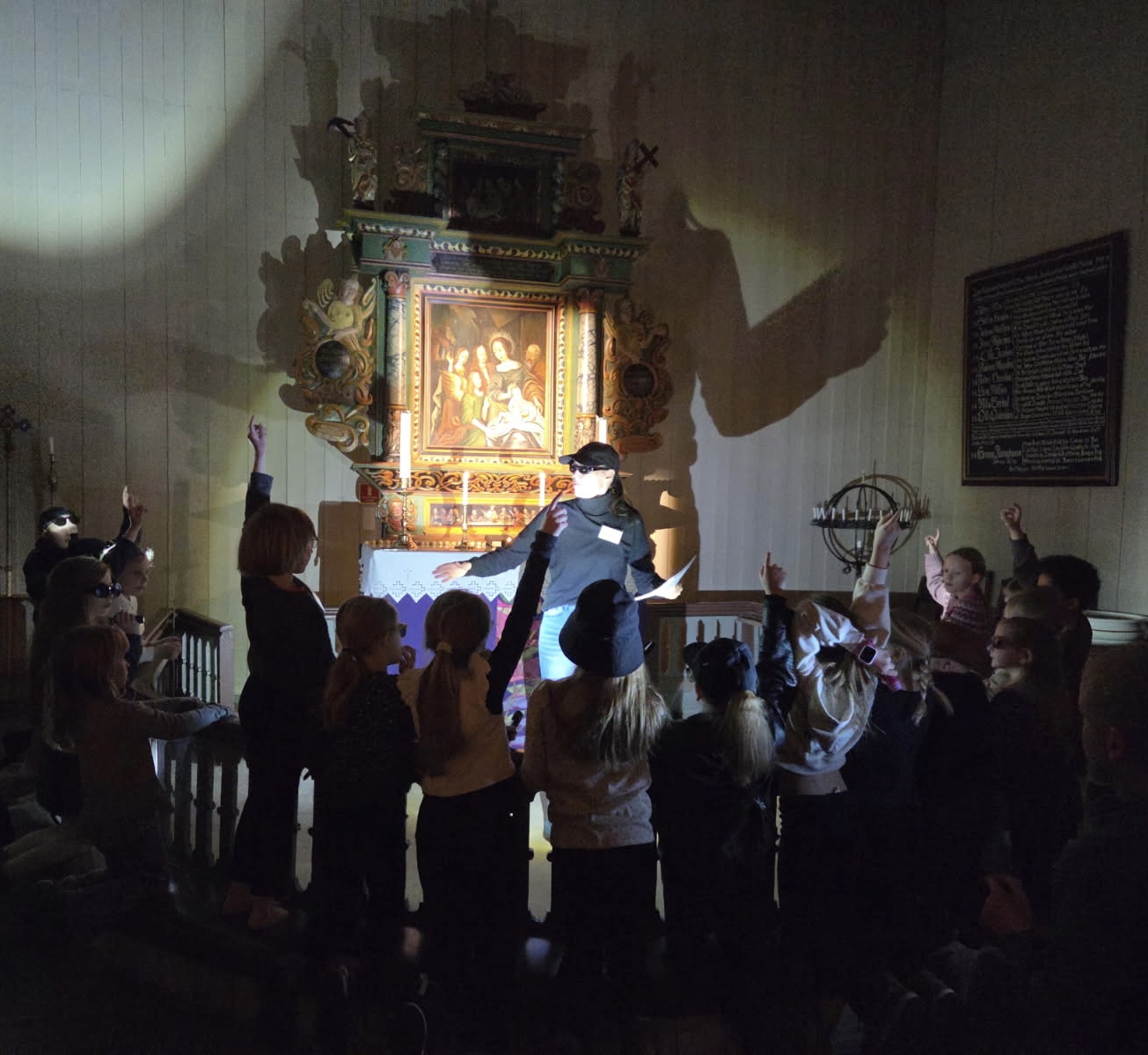 Person i silhuett mot alterringen i en mørk kirke med barn rundt alterringen