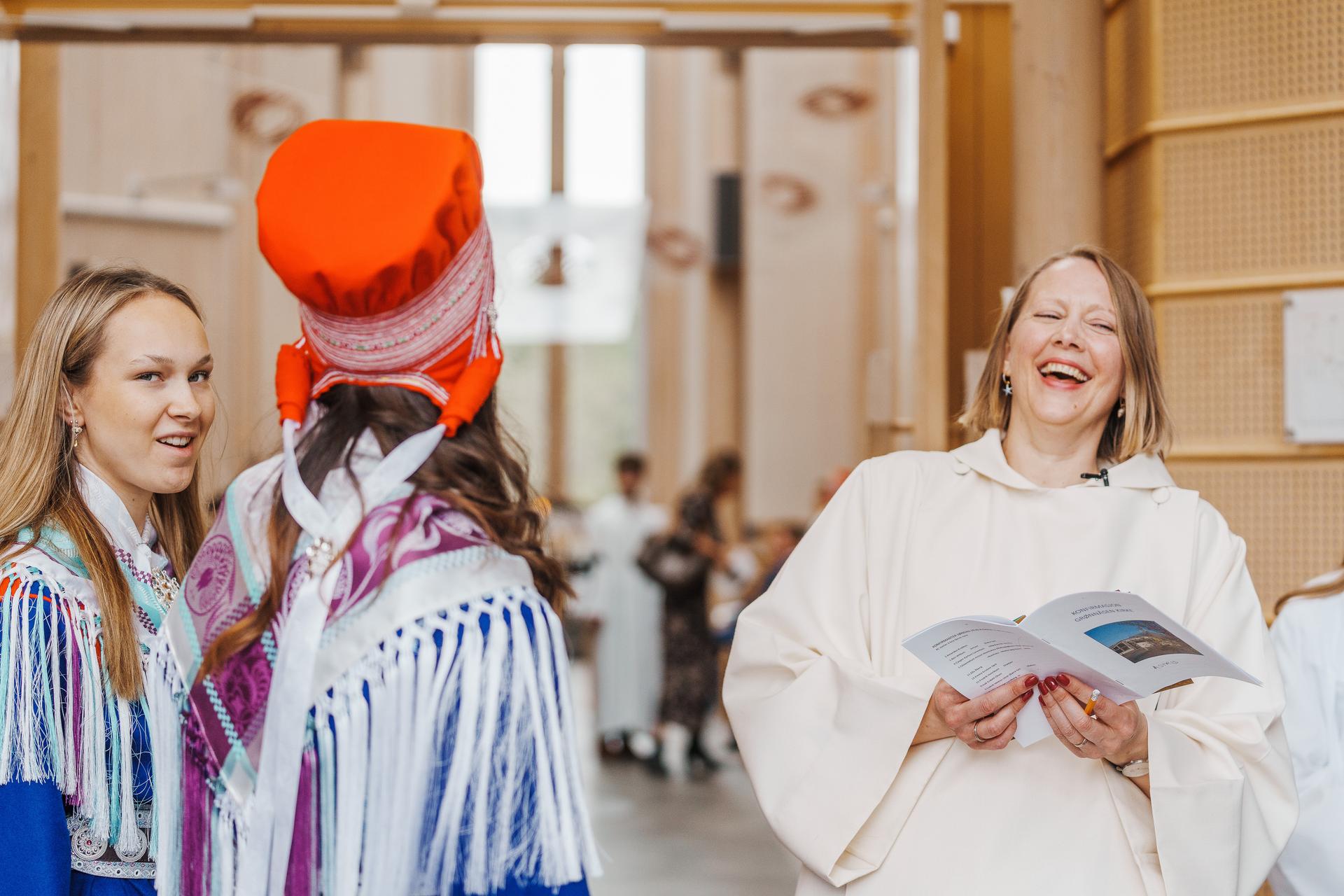 Portrett av Menighetspaedagog som ler hjertelig mens hun snakker med to jenter i samisk drakt