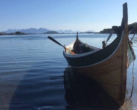 Bildet er av en gammel trebåt i sola på vannet med horisont bak